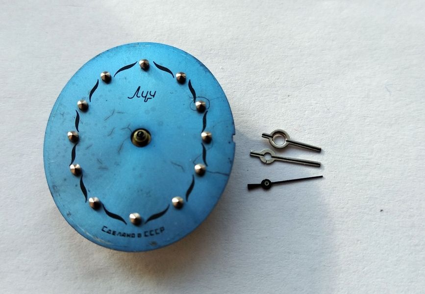 Blue Luch dial with its three hands removed and laid beside it
