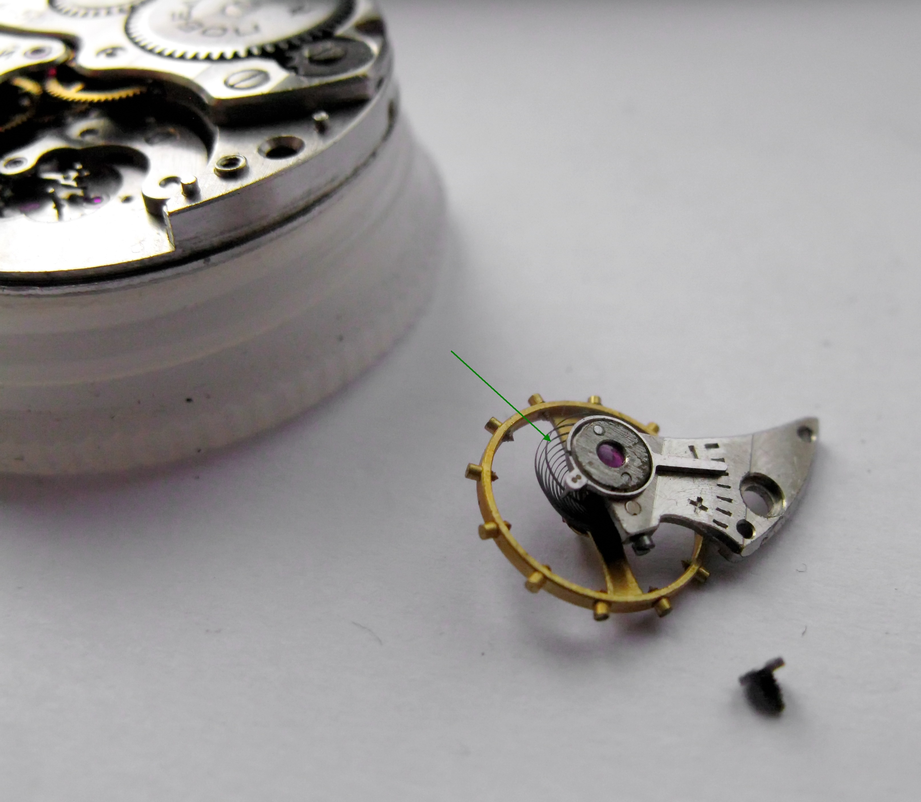The balance removed and set aside, with a green arrow pointing to the raised Breguet overcoil of the hairspring.