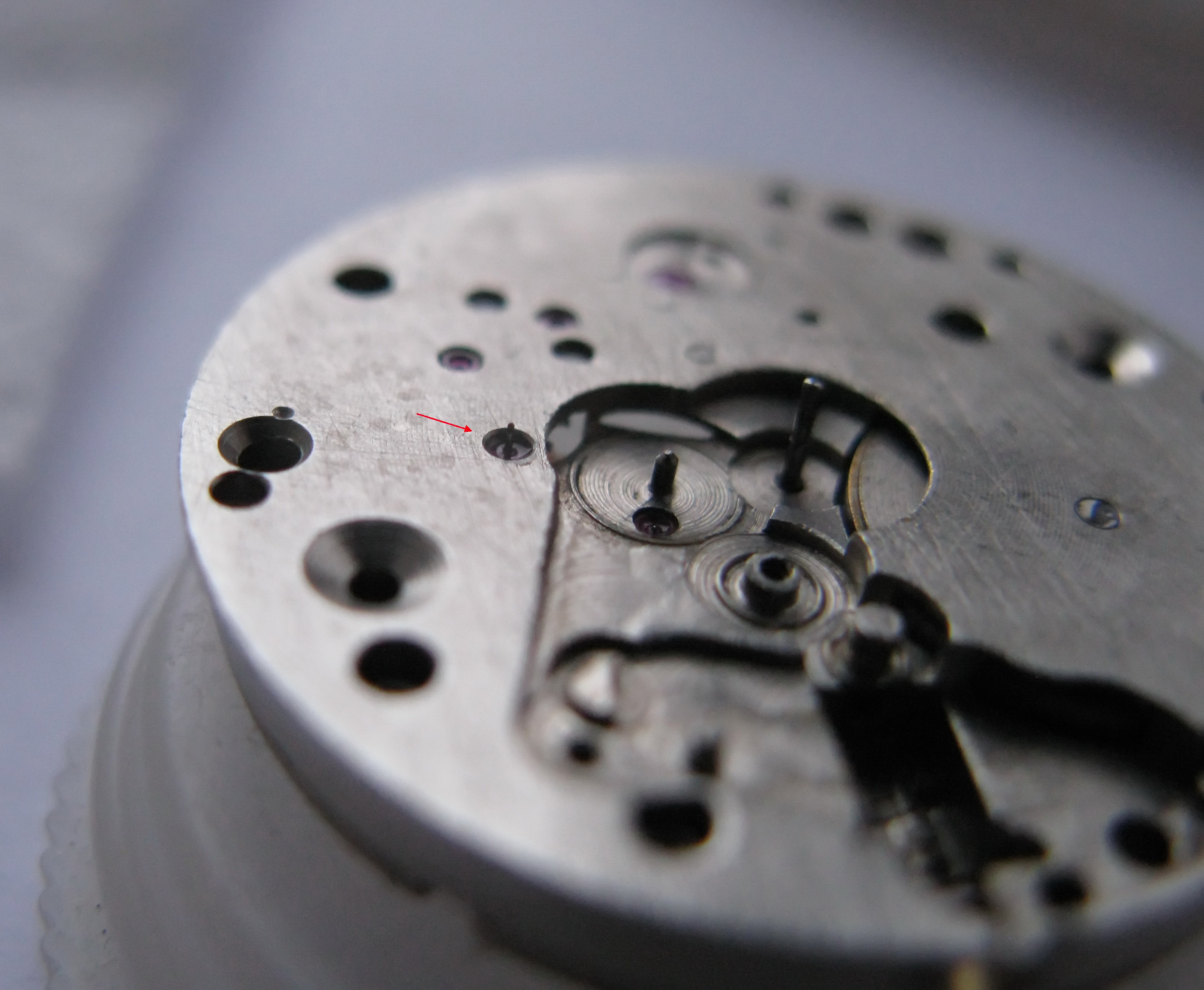 The movement with a red arrow indicating the seconds-wheel arbor that carries the seconds hand.