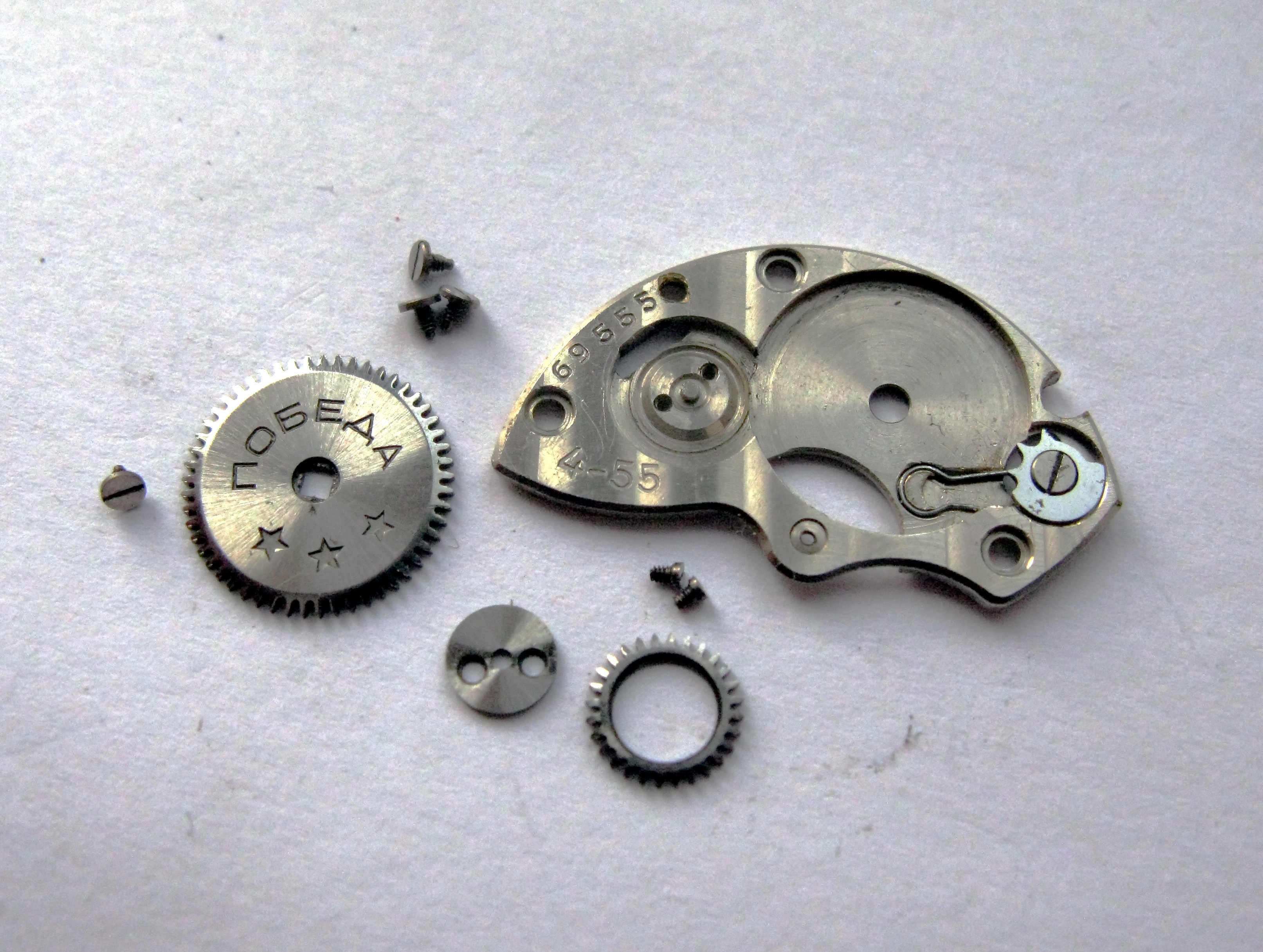 The winding mechanism disassembled, showing the Pobeda-engraved ratchet wheel, sliding clutch parts and barrel bridge.