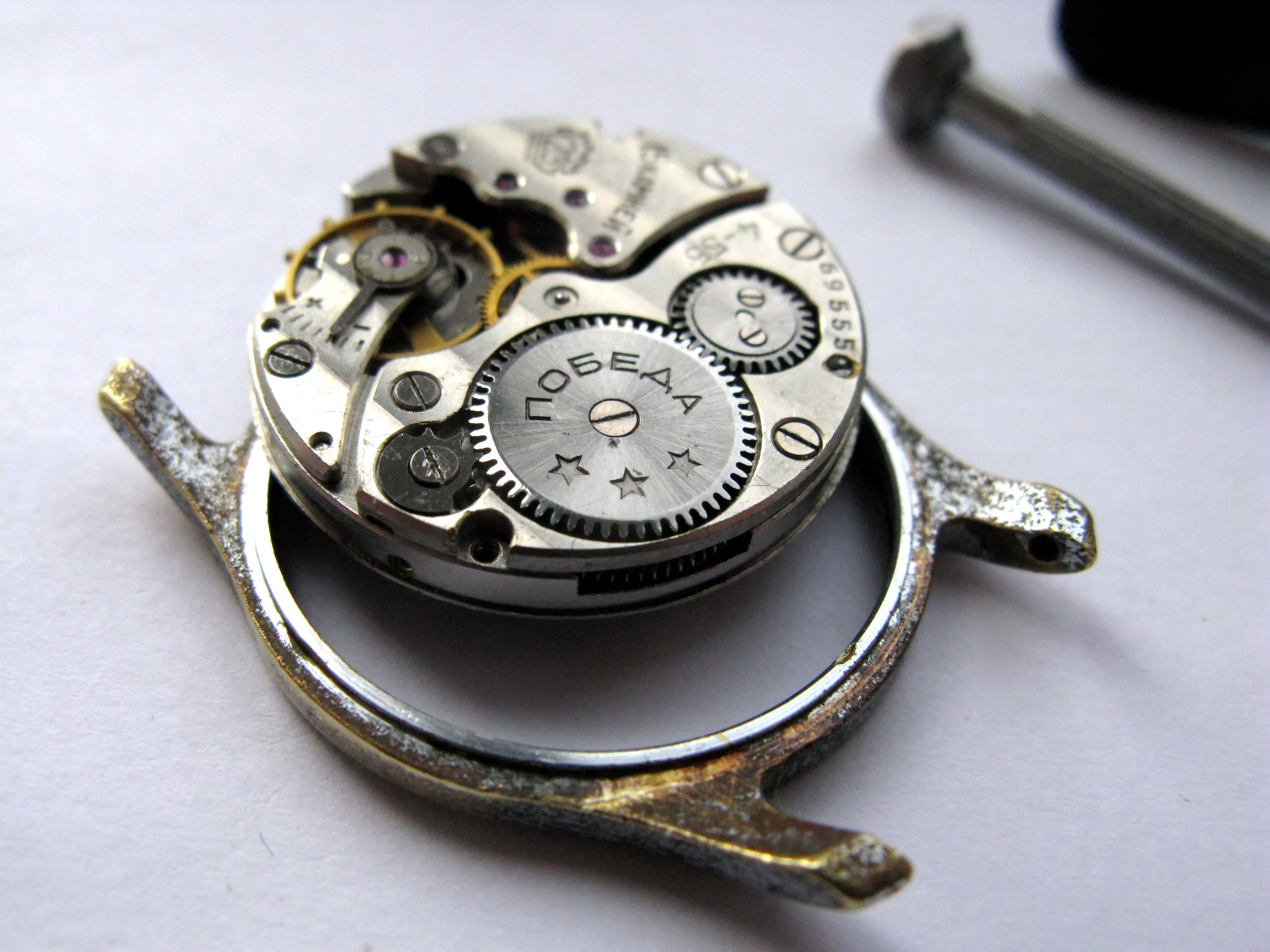 The movement removed from the case, showing Geneva stripes and the Pobeda engraving, with the case ring beside it.