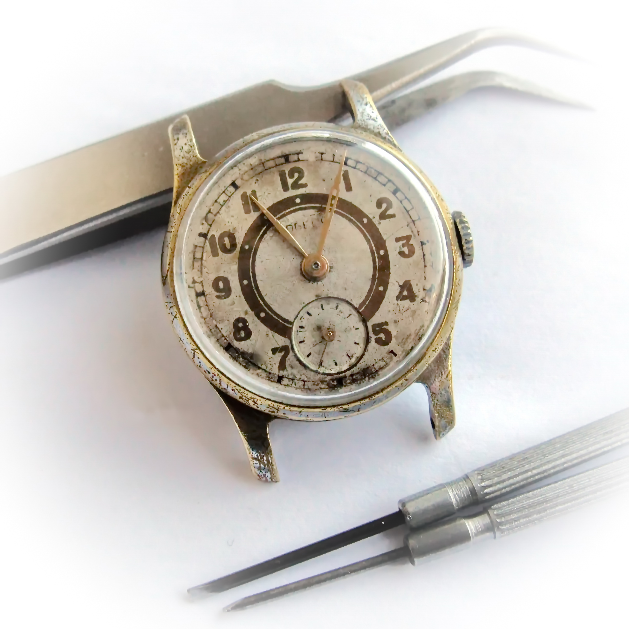 The serviced Pobeda watch, cased and running, beside watchmaker's tweezers and a screwdriver.