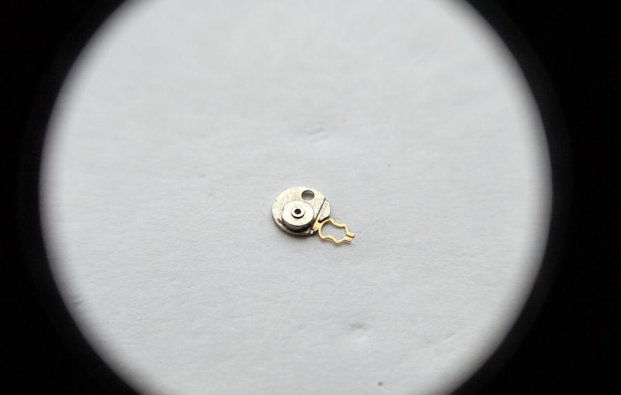 The underside of the balance bouchon setting showing grooves that capture the arms of the lyre spring