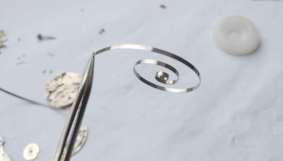 The cleaned S-shaped mainspring uncoiled on the bench