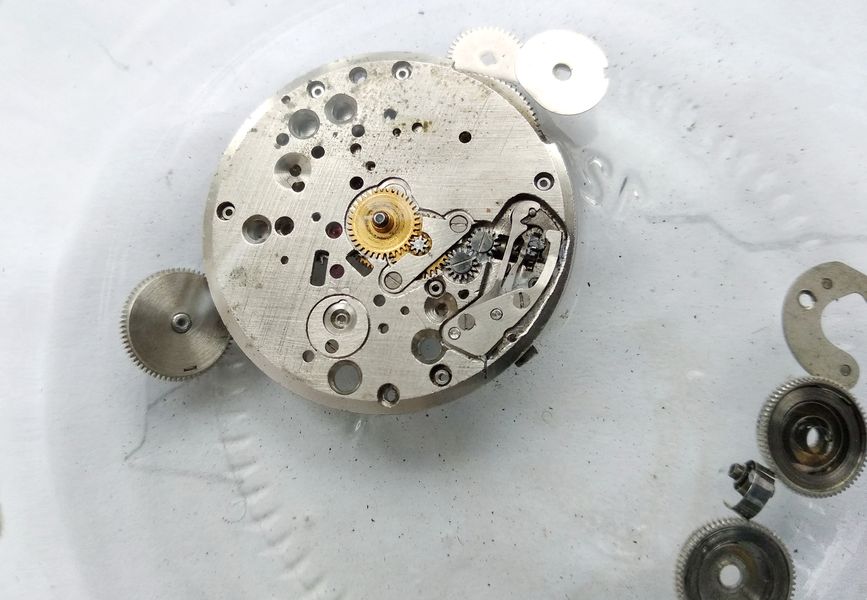 The assembled main plate submerged in a benzine bath alongside other parts