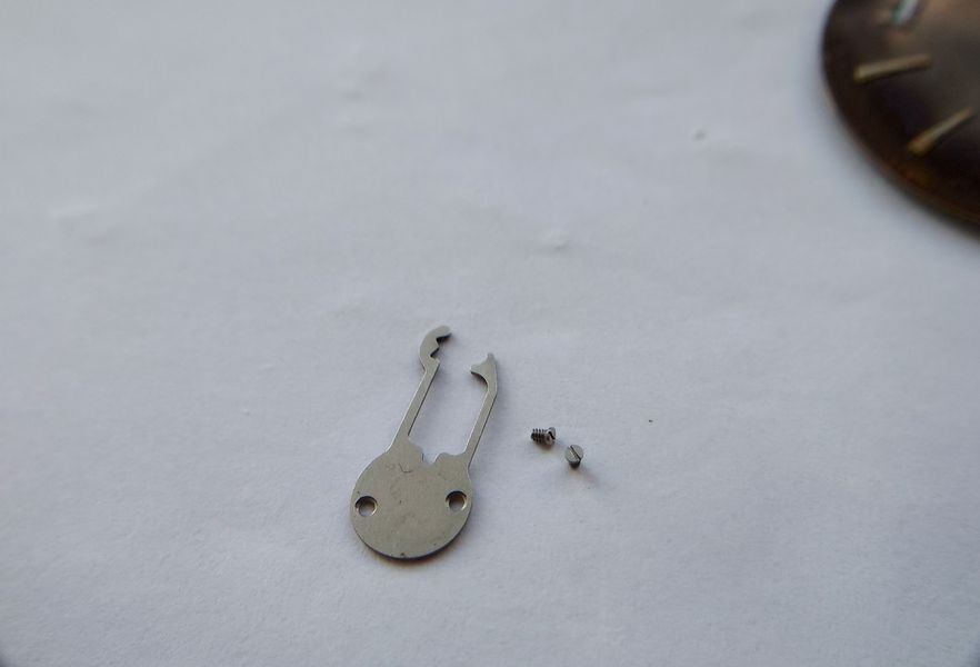 Spring cover plate for the Raketa 2609B keyless works being removed, showing its complex formed profile with multiple bends