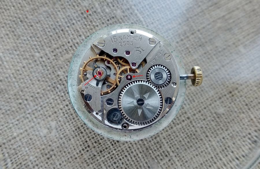 Raketa 2603 movement with arrows indicating the Incabloc bouchons on the balance assembly and the jeweled center wheel pivot in the barrel bridge