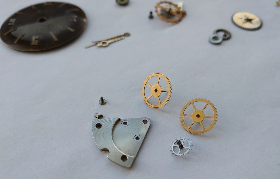 Gear train wheels from the Raketa 2609B removed and laid alongside the sector bridge, overlay cap jewels visible on the bridge underside