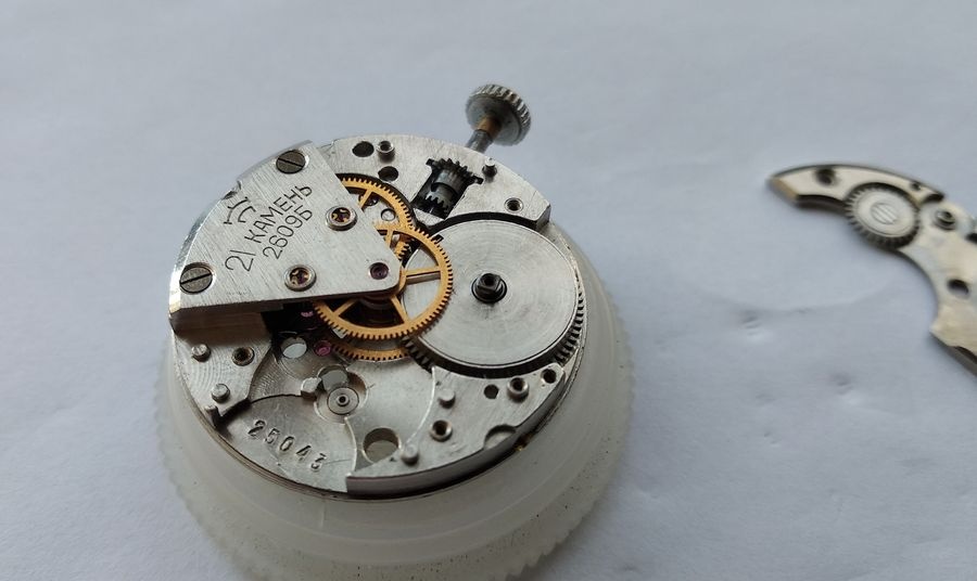 Serviced mainspring barrel of the Raketa 2609B being installed in the main plate, barrel arbor pivot seated in the center wheel bridge jewel below