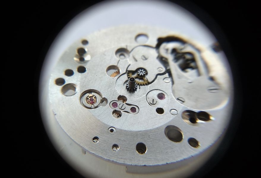 Overlay cap jewels reinstalled on the Raketa 2609B gear train bridge with their retention springs, cannon pinion being fitted to the center wheel arbor
