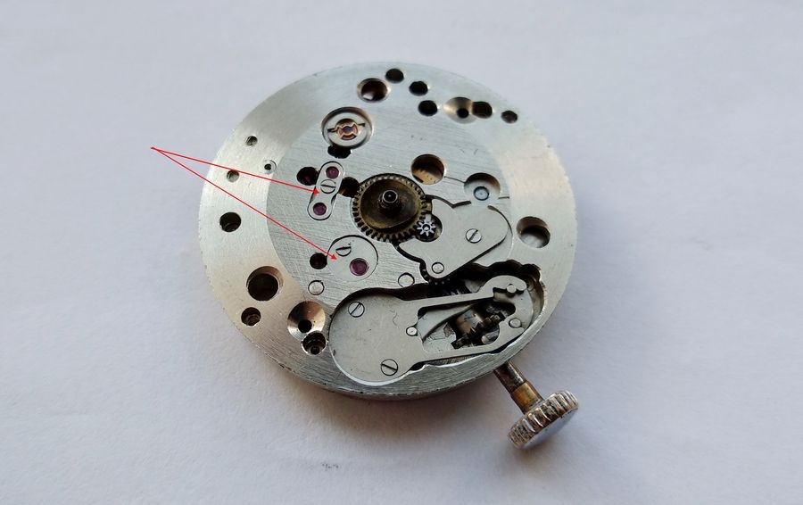 Under-dial view of the Raketa 2609B showing beveled main plate edges and overlay jewels covering gear train pivot positions, key features indicated by arrows
