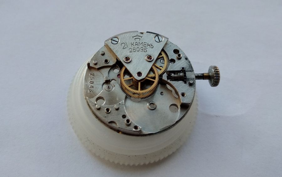 Raketa 2609B gear train bridge being released and lifted, showing the sector profile and the single-side cantilevered mounting