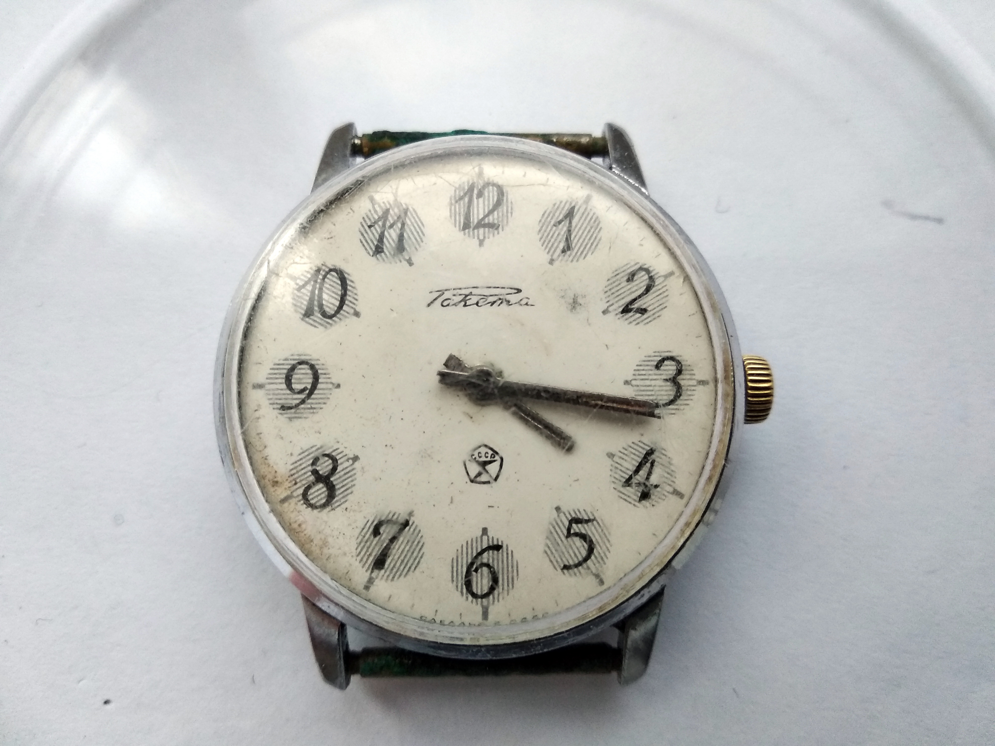 Front of a grimy Raketa wristwatch with a heavily worn crown and a stained dial bearing the Soviet Quality Mark