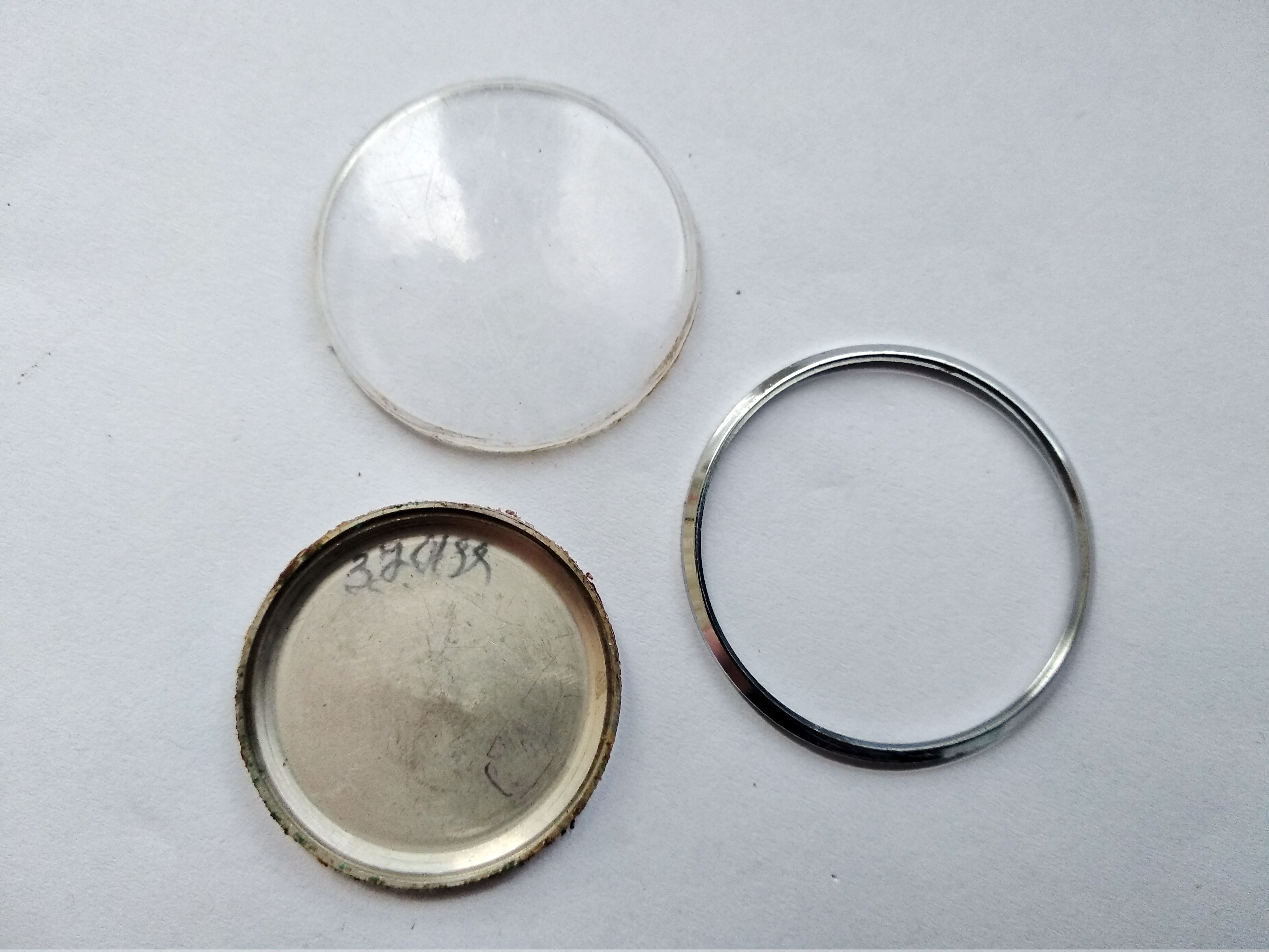 Bezel and acrylic crystal separated from the case, with the caseback showing an old service mark