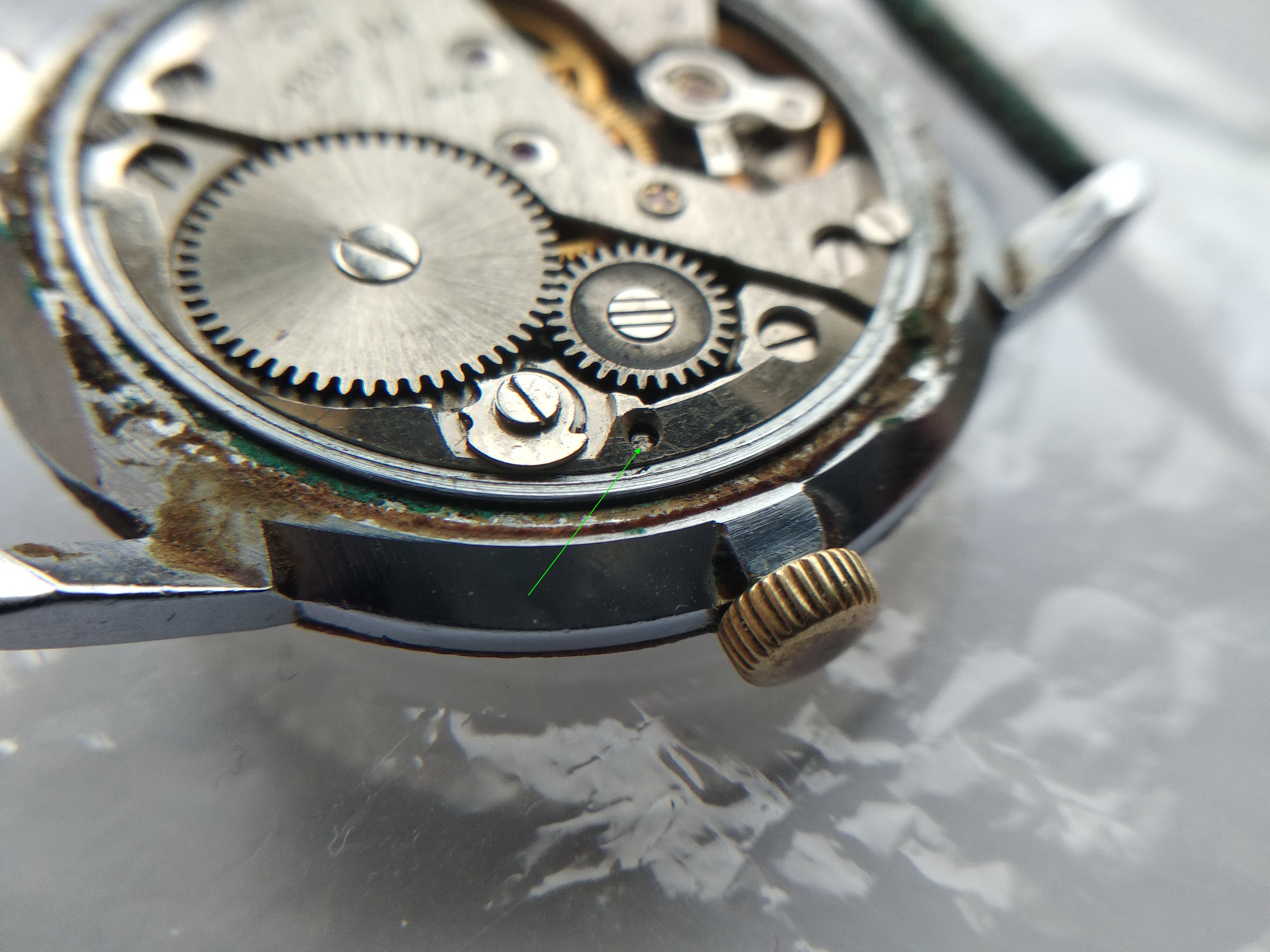 Movement with a green arrow marking the keyless-works release button pressed to free the stem