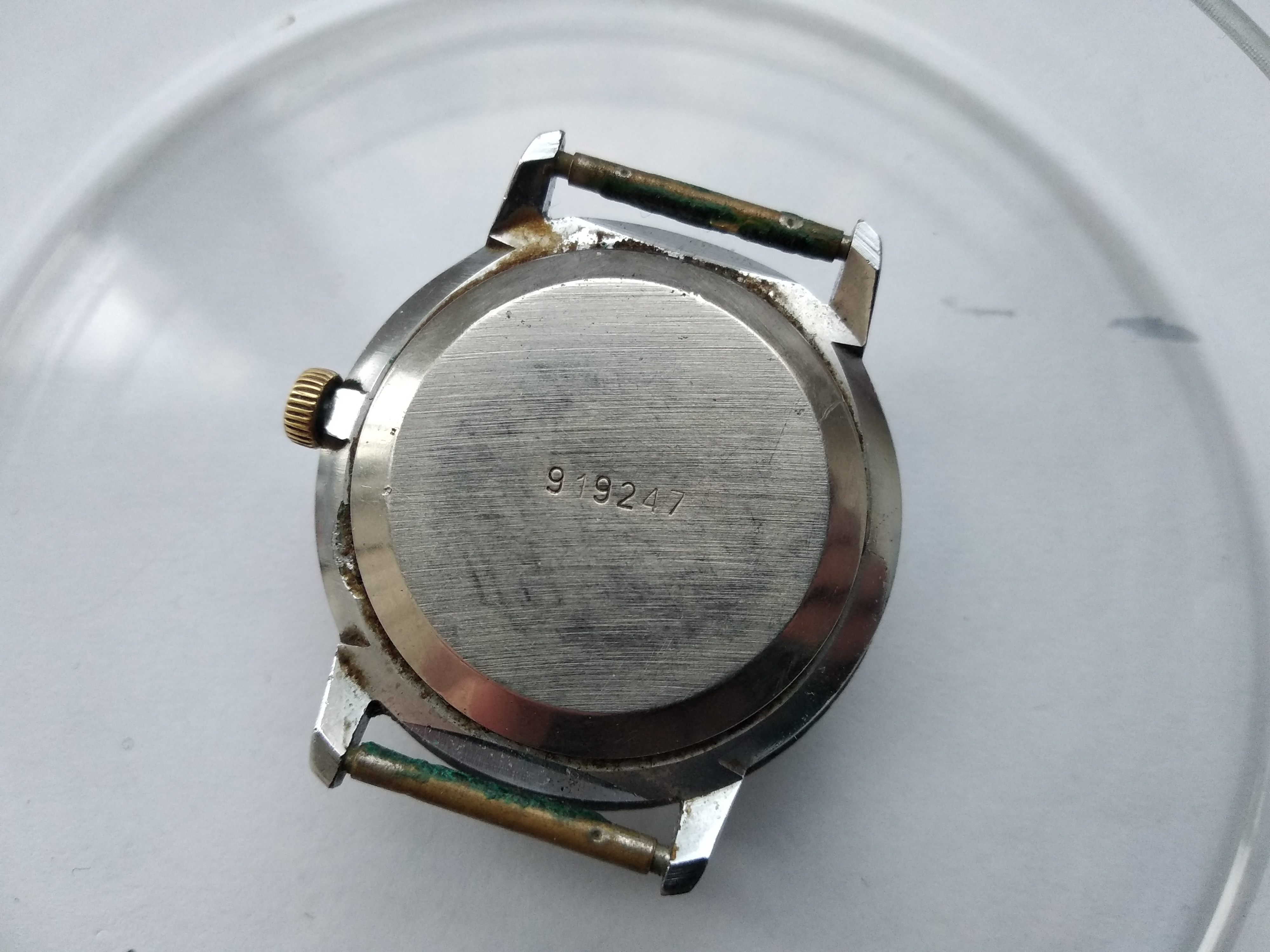 Caseback of the Raketa covered in dirt, with a filed flat on the case edge used as a pry point