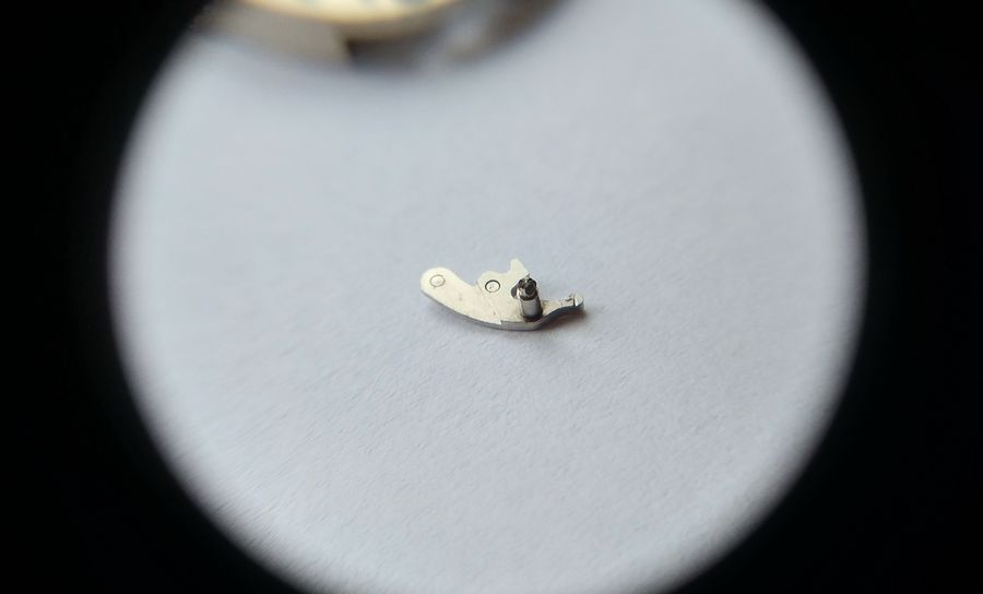 The reverse face of the intermediate lever under a loupe, showing the stem-release push-button pin