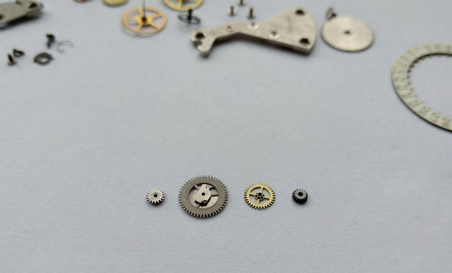 The removed calendar parts laid out on the bench — several wheels, the bridge, the date disc edge and small screws