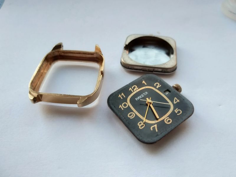 The gilt dial fitted with hands beside the gold case middle and the old corroded caseback