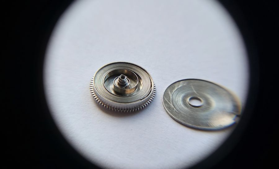 A loupe view of the barrel with its mainspring fitted inside, the barrel lid lying beside it