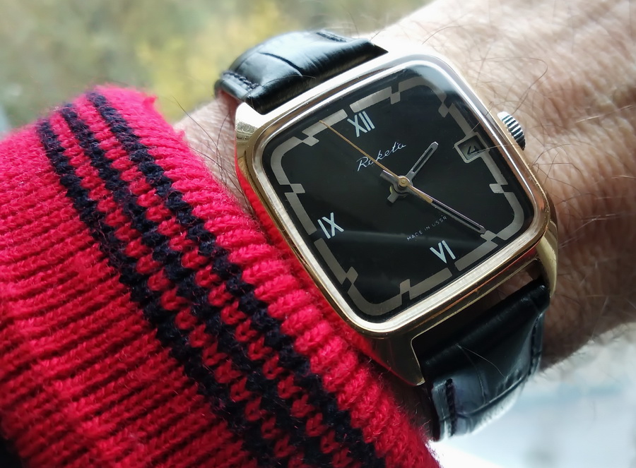 The gold version with a black Roman-numeral dial worn on the wrist over a red sleeve