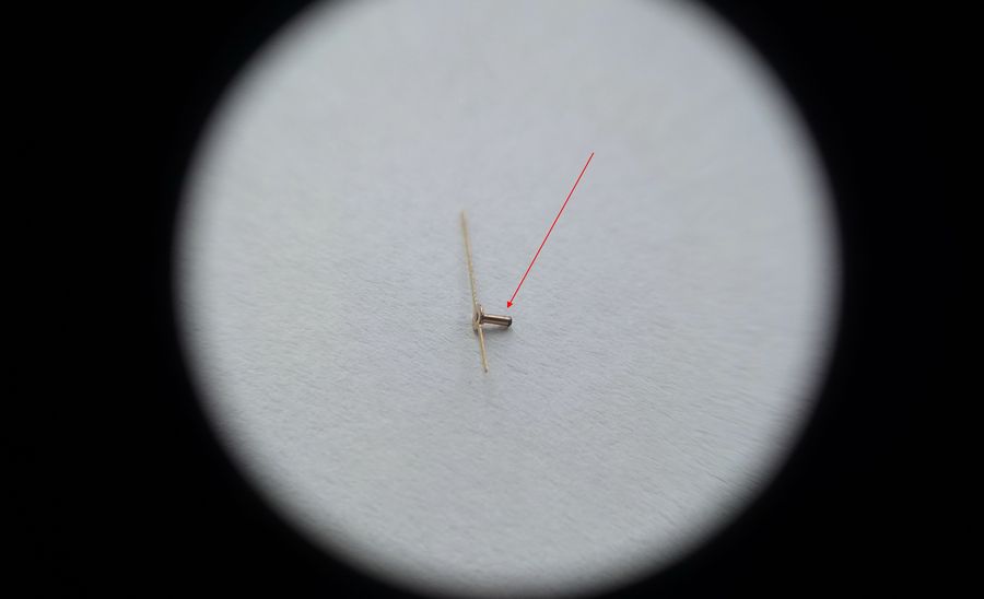 A single central seconds hand with an unusually long mounting pipe under a loupe, a red arrow pointing to the pipe