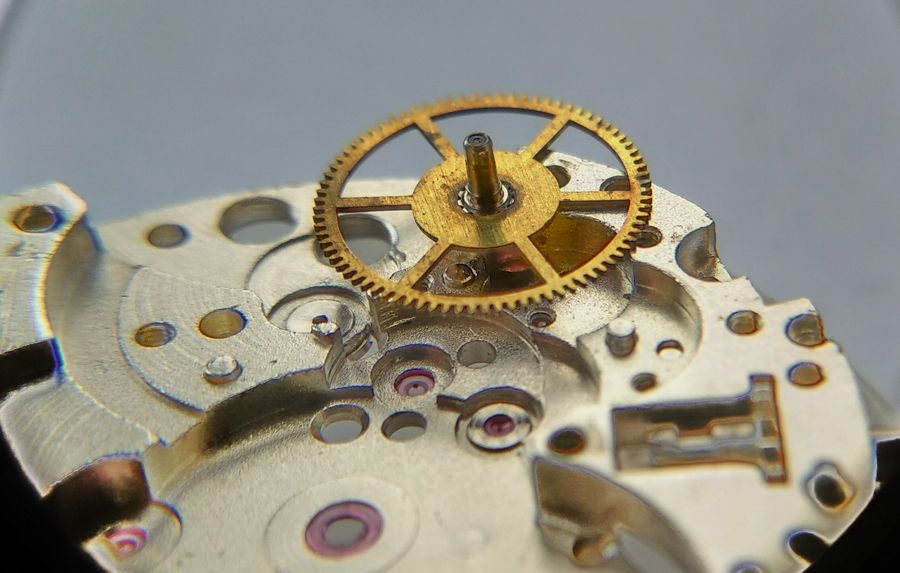 The center wheel held in tweezers, showing aged surfaces but clean pivots