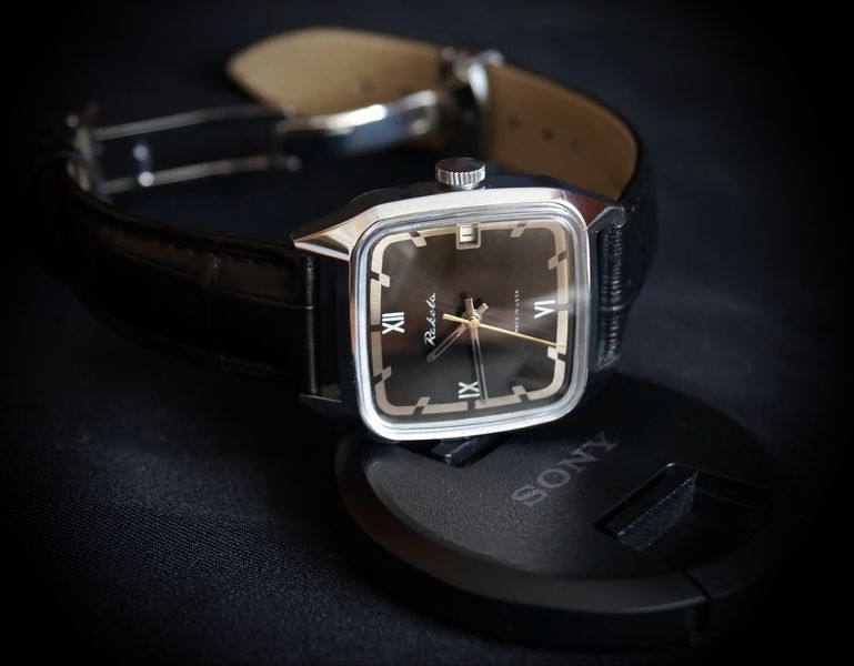 The chrome version resting at an angle on a black camera lens cap under low-key lighting