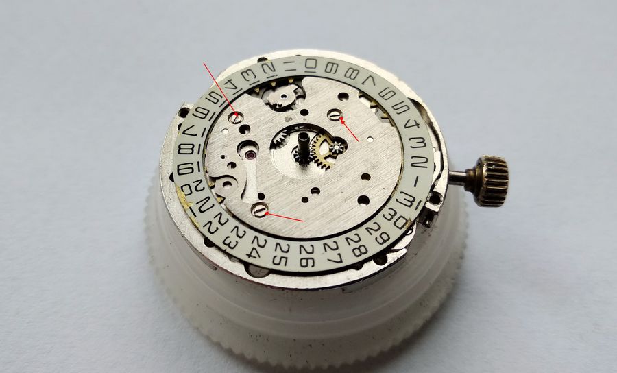 A screwdriver at one of three small screws securing the calendar bridge on the dial side