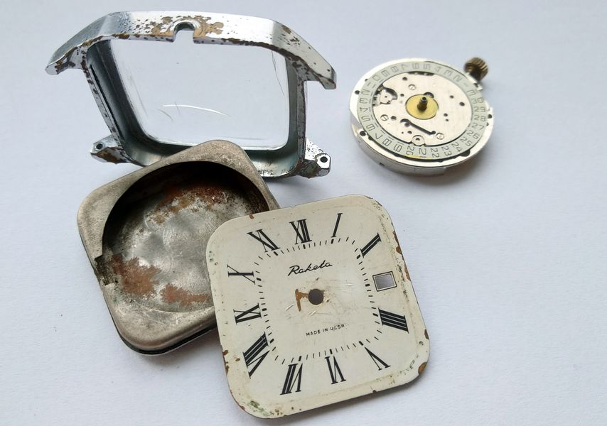 Corroded square bezel with crystal, a rust-stained caseback, the Raketa dial, and the movement, all separated on a light background