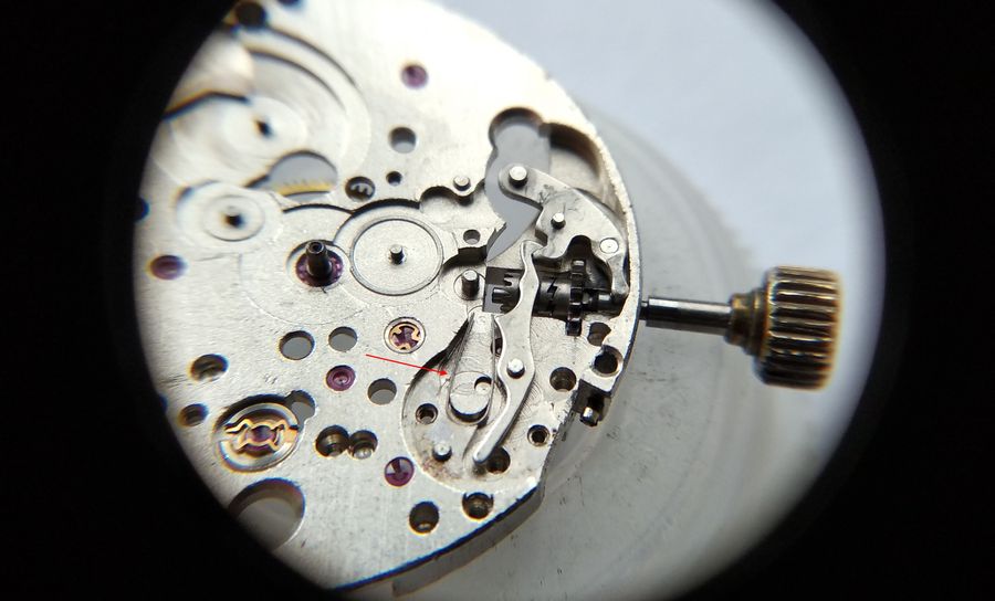 A loupe view of the keyless works with a red arrow pointing to the misplaced U-shaped spring