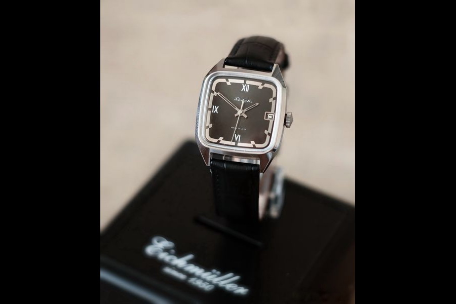 The chrome-cased white version of the watch with a dark dial displayed on a stand