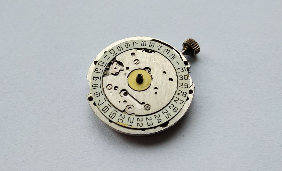 Dial side of the movement showing the printed date ring around the calendar plate, with the winding stem and crown attached