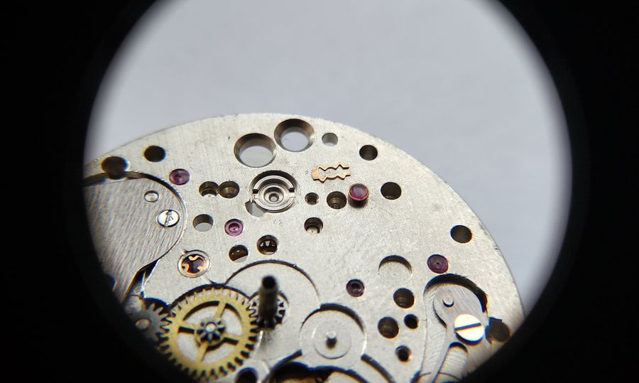 The lyre-shaped shock spring and the cap-jewel setting being removed from the balance bearing