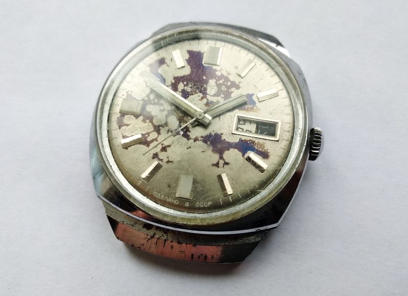 Front of a Vostok watch with a heavily stained silver dial, applied markers, and a day-and-date window at three o'clock
