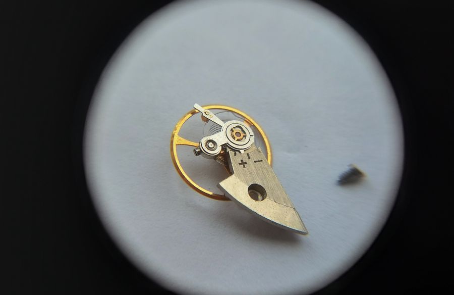 Oblique magnified view of the balance cock underside showing the plus-minus regulator and stud carrier