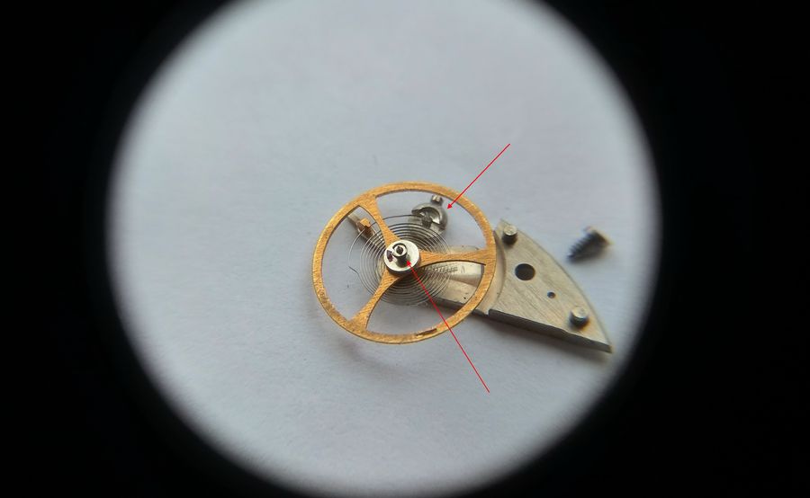 Magnified view of the gilt three-arm balance and cock with arrows indicating the heel and stud