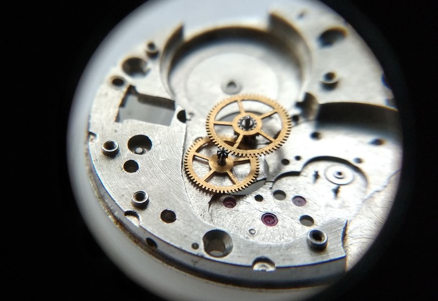 Vostok 2605 movement dial side through loupe showing intermediate wheel fitting beneath center wheel in main plate