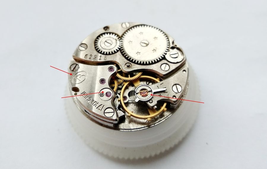 Vostok 2605 movement on holder bridge side with two red arrows indicating incabloc lyre spring and escape wheel overlay jewel