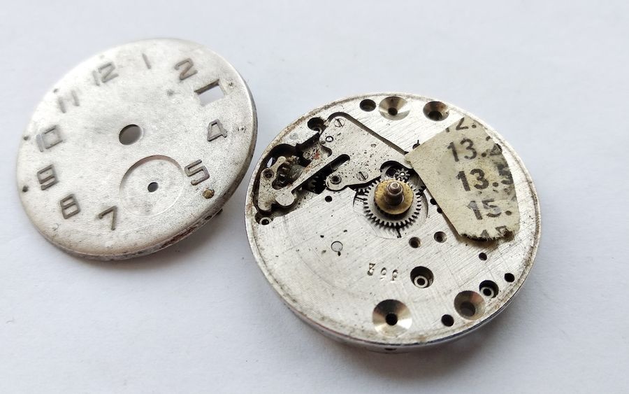 Vostok 2605 movement dial-side with newspaper clipping substituting missing calendar disc visible in calendar mechanism recess