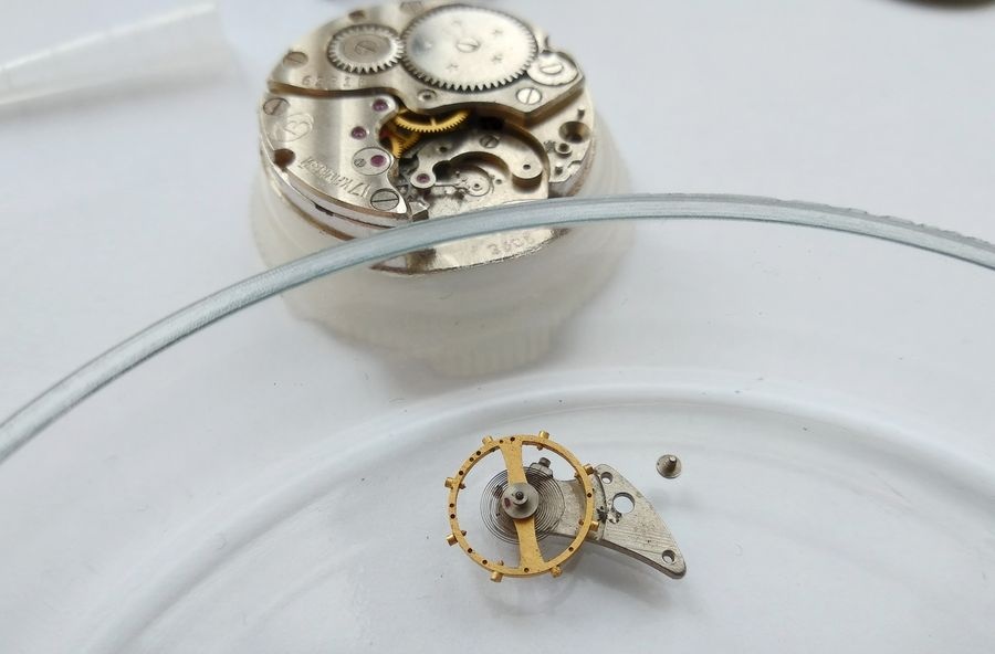 Vostok 2605 movement on holder with balance assembly removed and placed in watch glass Petri dish below