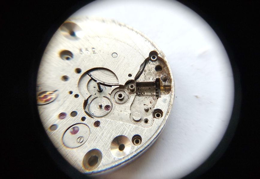 Vostok 2605 keyless works disassembled through loupe showing heavy dirt contamination in components