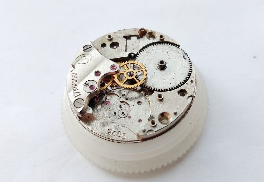 Vostok 2605 movement on holder with barrel bridge removed and going train wheels visible with contamination