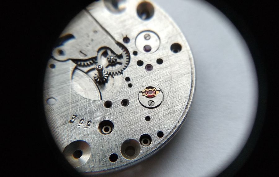 Vostok 2605 dial side through loupe showing bouchon reinstalled in main plate with lyre spring tail in groove