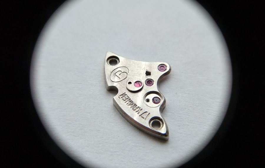 Vostok 2605 gear train bridge through loupe with overlay jewel of escape wheel removed and MBP-12 oil drop visible on jewel