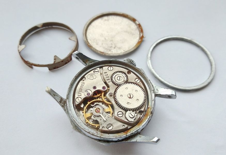 Vostok 2605 movement visible in case after gasket removal with threaded retaining ring and movement holder ring set alongside
