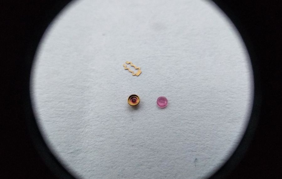 Vostok 2605 balance cock bouchon components through loupe showing lyre spring bouchon carrier and cap jewel laid out for service