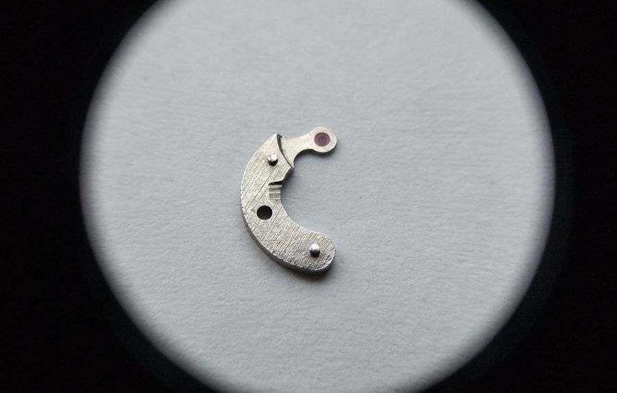 Vostok 2605 pallet fork bridge outer face through loupe showing mounting holes and jewel position