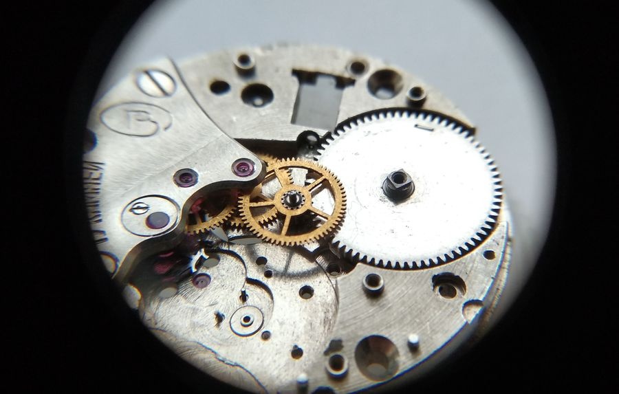 Vostok 2605 movement through loupe with barrel installed alongside gear train bridge ratchet wheel visible