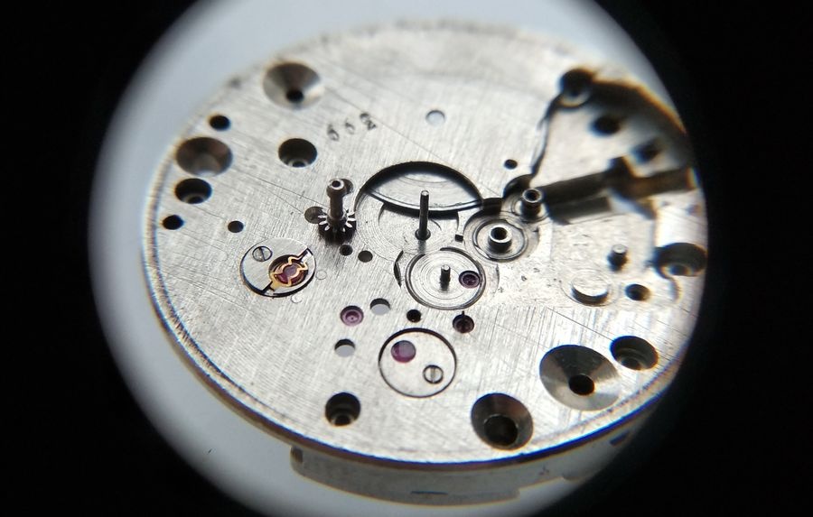 Vostok 2605 dial side through loupe with cannon pinion being prepared for installation on center wheel post before transfer wheel